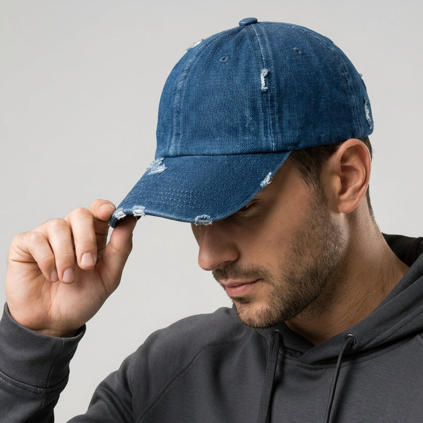 Man wearing a blue distressed cap with a gold logo on a gray background