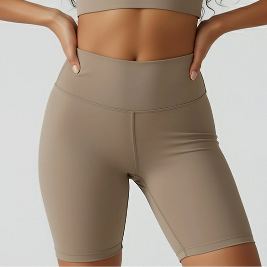 Woman wearing a beige sports bra and shorts on a plain background