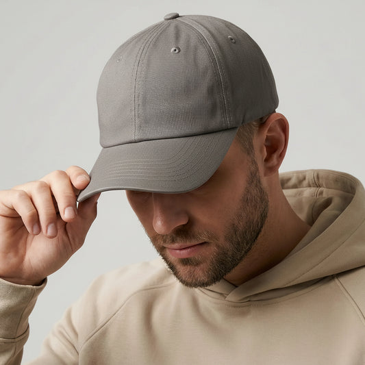 Man wearing a gray cap with a brand tag, looking down, on a plain background