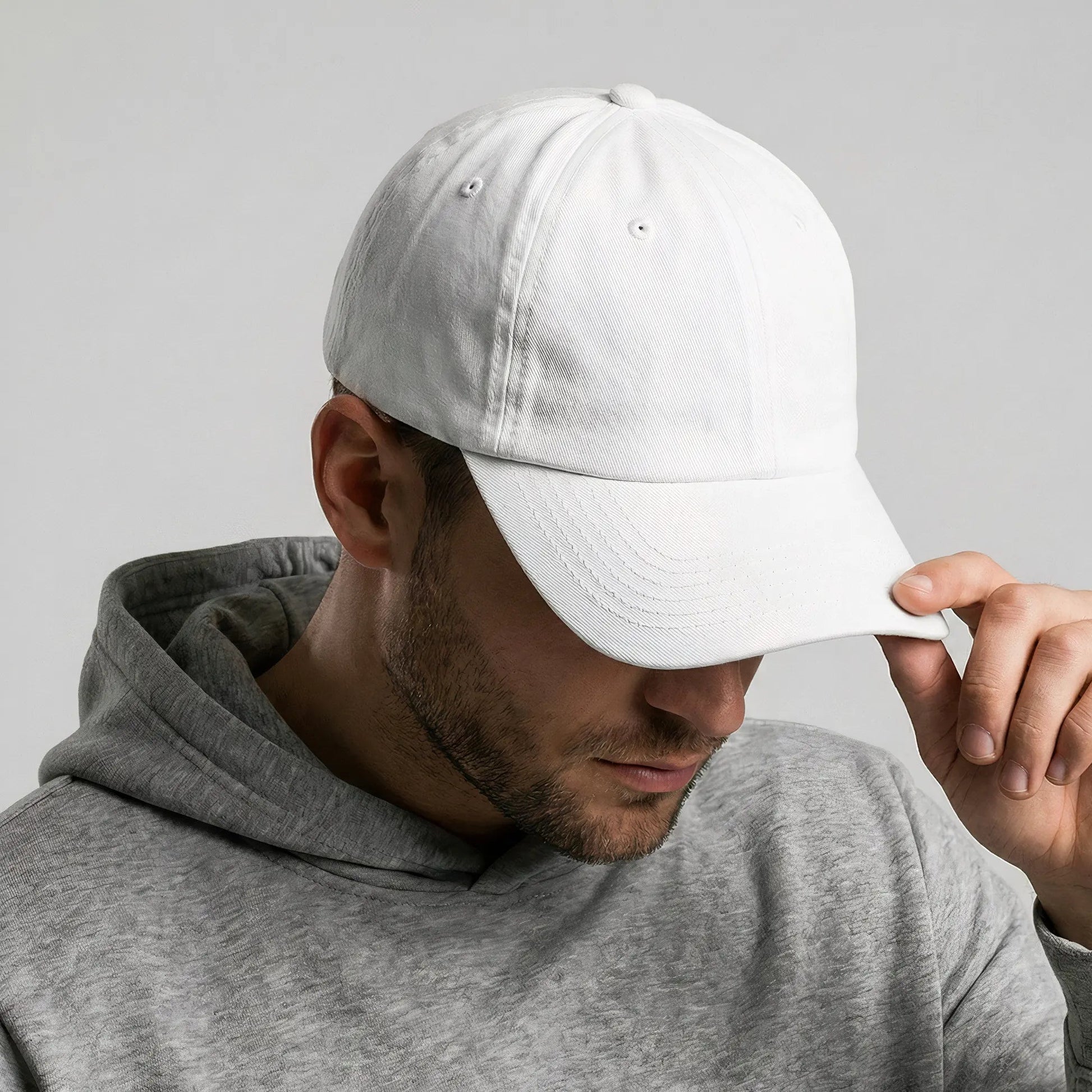 Man wearing a white cap and gray hoodie against a plain background