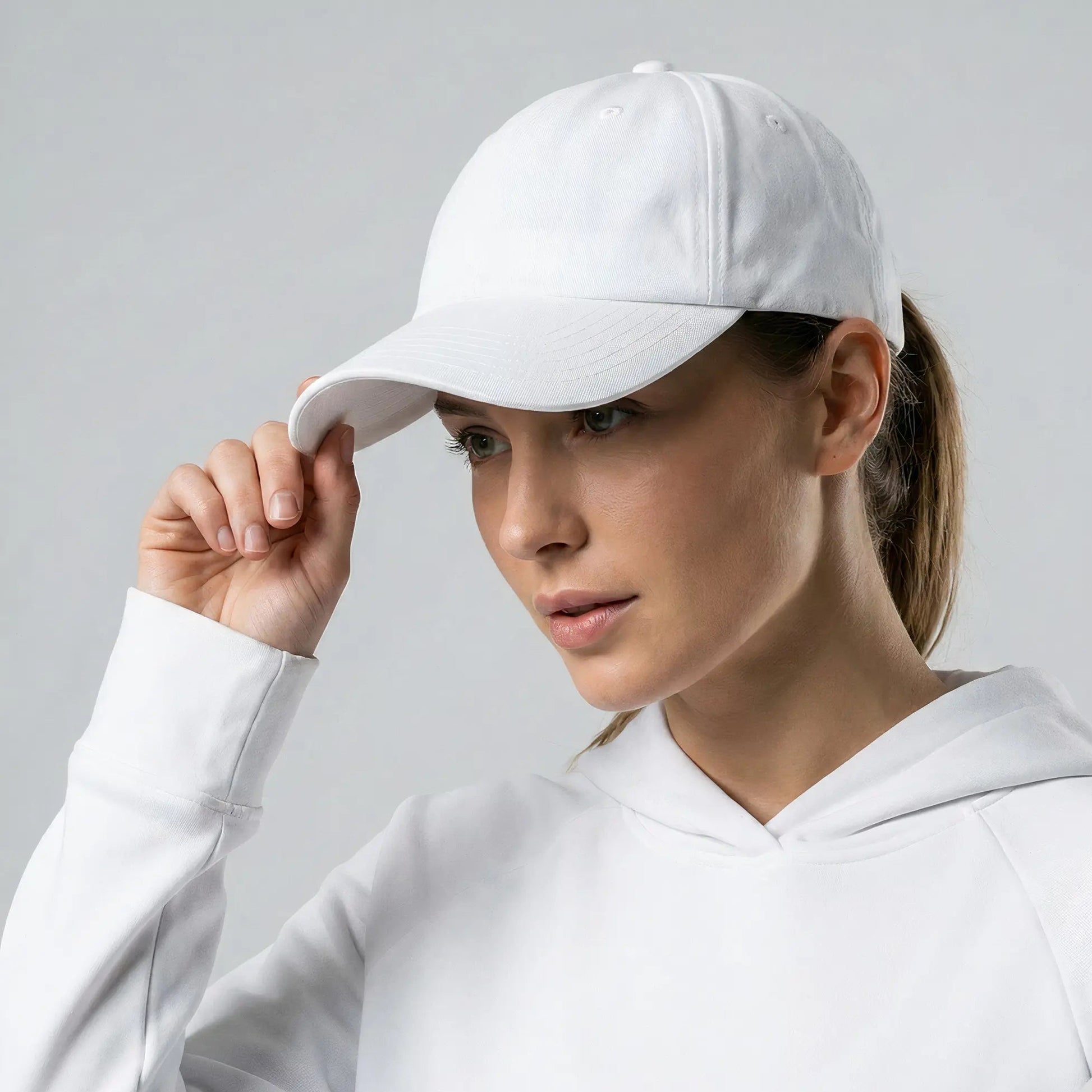 Woman wearing a white cap and hoodie against a gray background