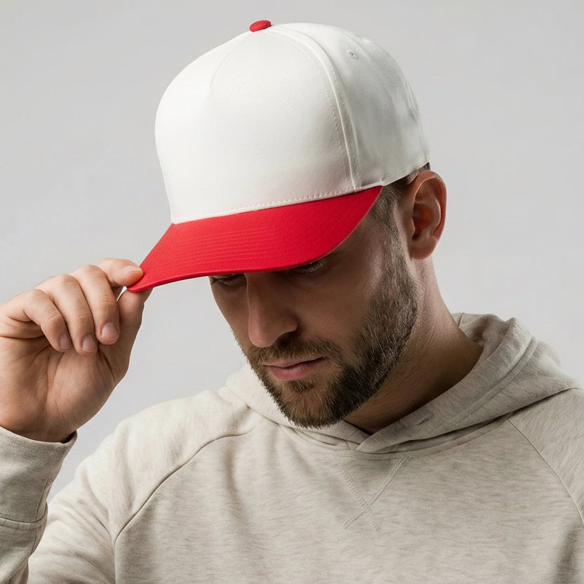 Man wearing a white and red cap with a logo, looking down, on a plain background