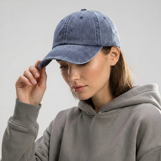 Woman wearing a gray hoodie and blue denim cap against a light gray background
