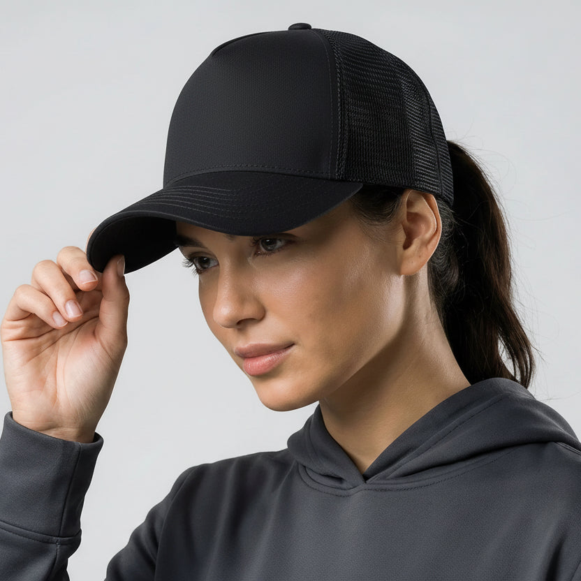 Woman wearing a black cap with a logo and a gray hoodie against a light gray background