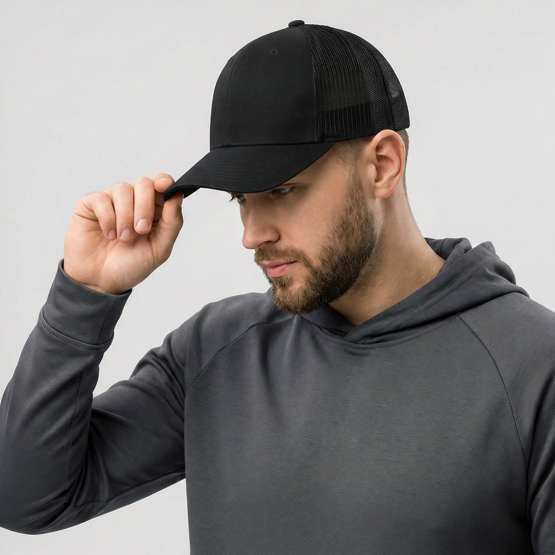 Man wearing a black cap and gray hoodie against a light gray background