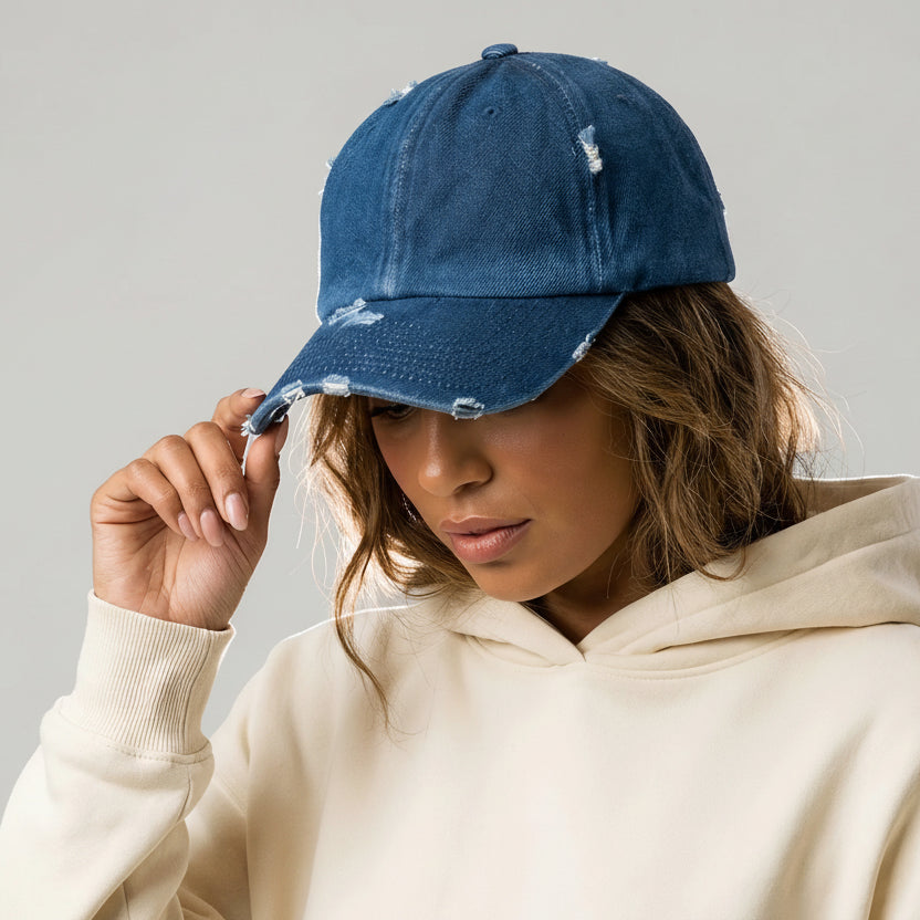Person wearing a blue denim cap with a logo and a beige hoodie on a gray background