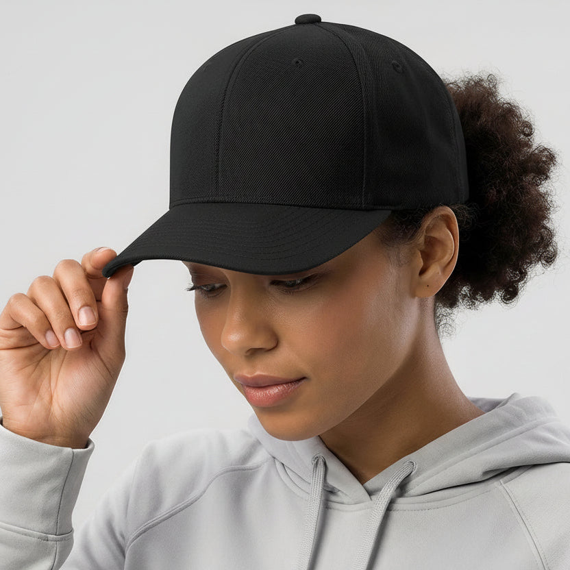 Woman wearing a black cap with a logo, holding it with her right hand against a light gray background.