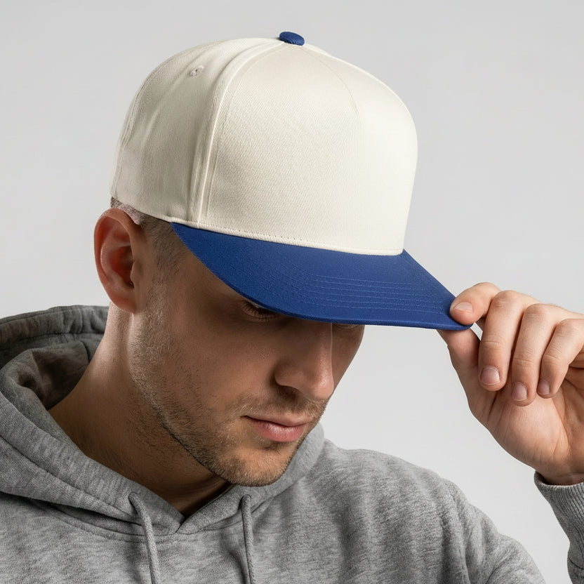 Man wearing a white and blue cap with a logo, looking down, on a light gray background