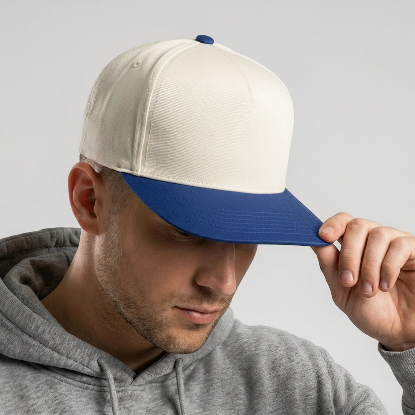 Man wearing a white and blue cap with a logo, looking down, on a light gray background