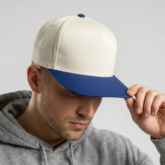 Man wearing a white and blue cap with a logo, looking down, on a light gray background