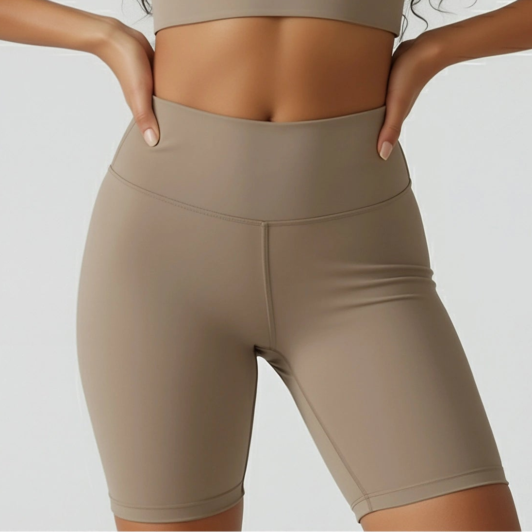 Woman wearing a beige sports bra and shorts on a plain background