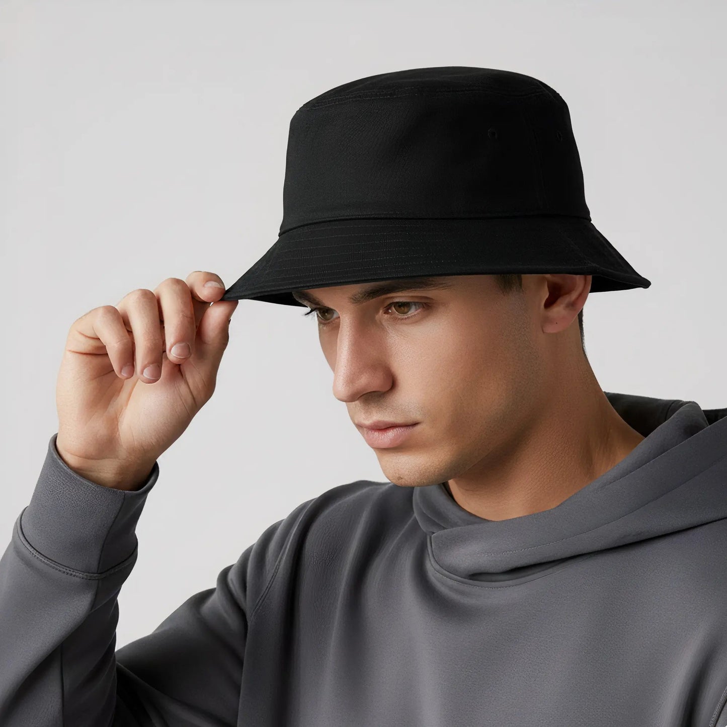 Man wearing a black bucket hat and gray hoodie against a light gray background