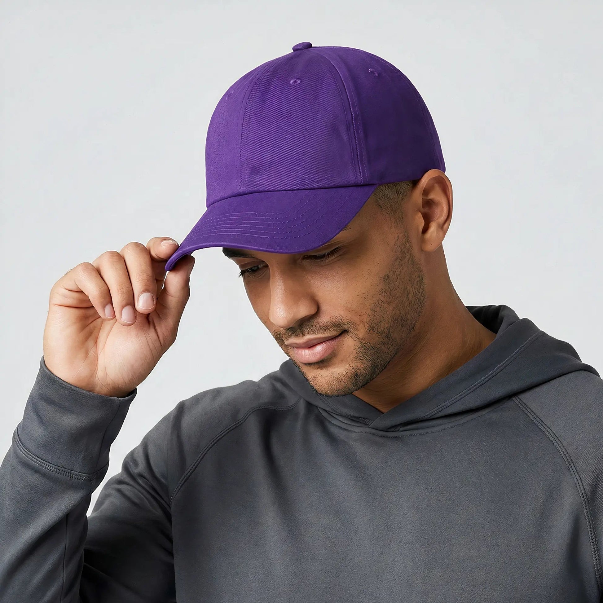 Man wearing a purple cap and gray hoodie against a light gray background
