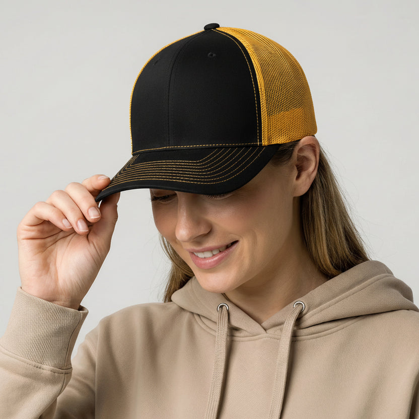 Person wearing a black and yellow cap with a rainbow sticker, holding it up to their face.