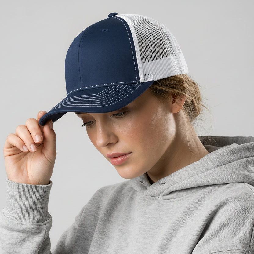 Person wearing a navy blue cap with a white mesh back and a gray hoodie on a light gray background