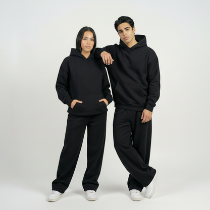 Two people wearing matching black hoodies and pants on a white background