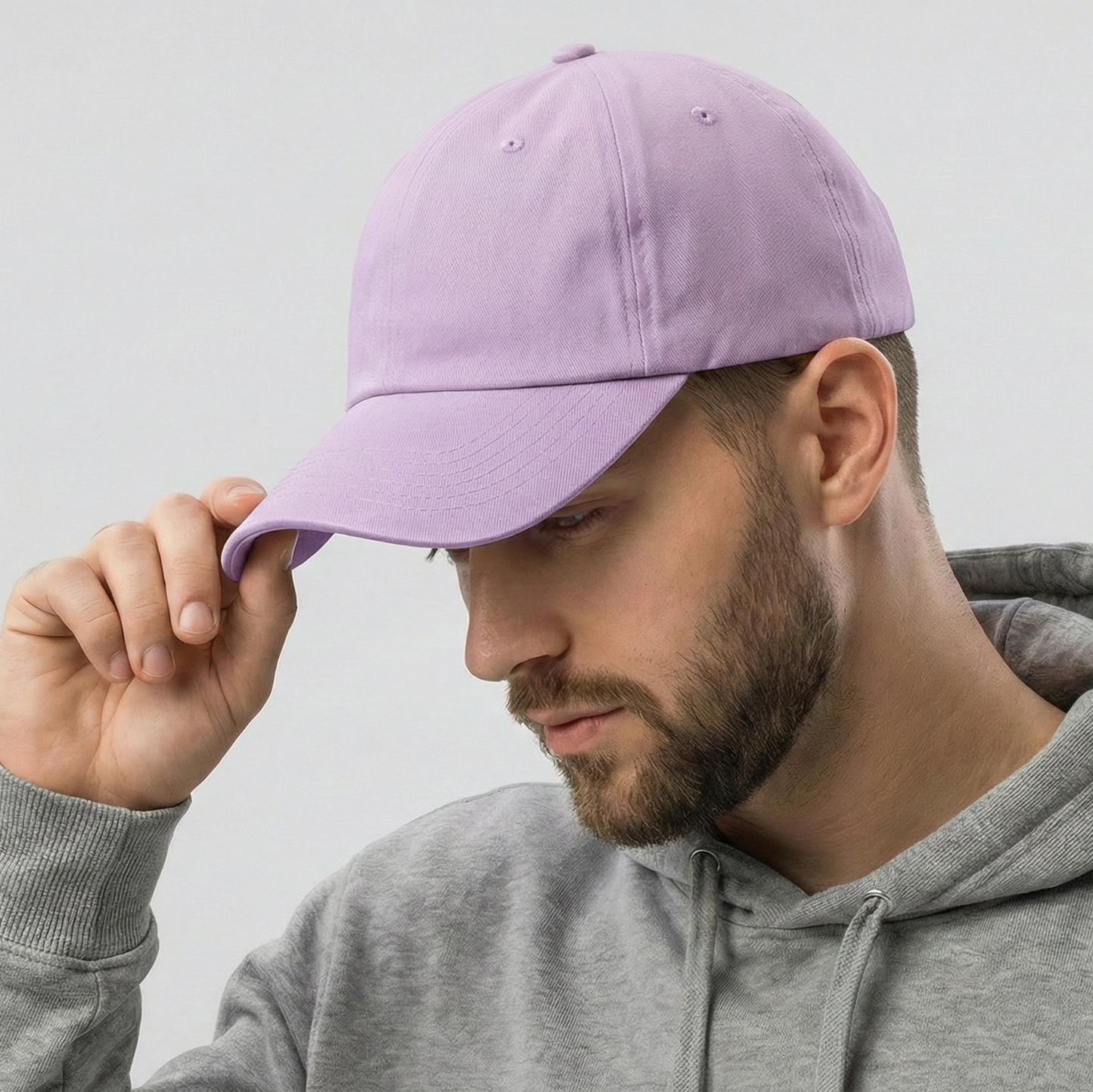 Man wearing a gray hoodie and holding a purple cap against a light gray background