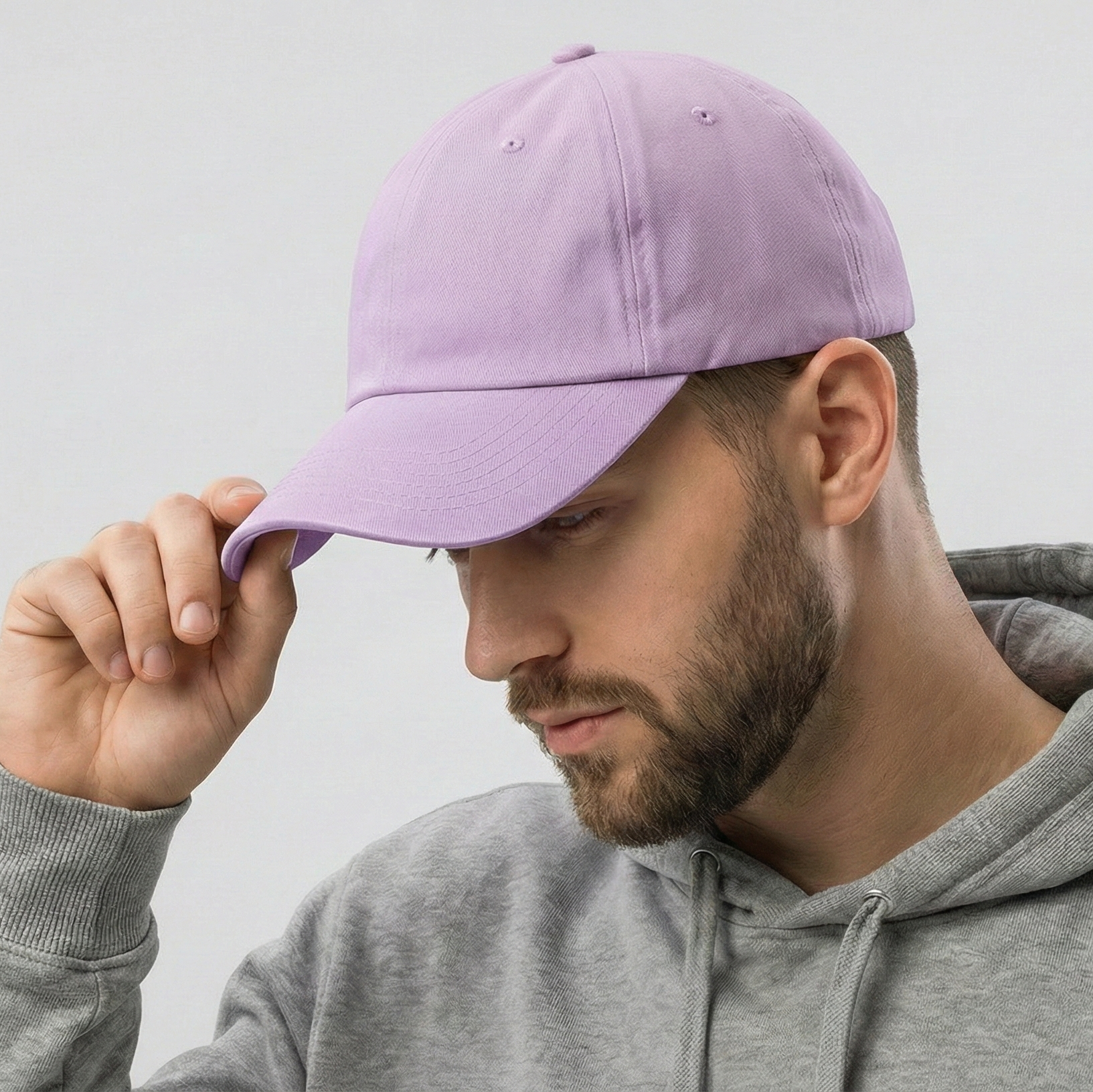 Man wearing a gray hoodie and holding a purple cap against a light gray background